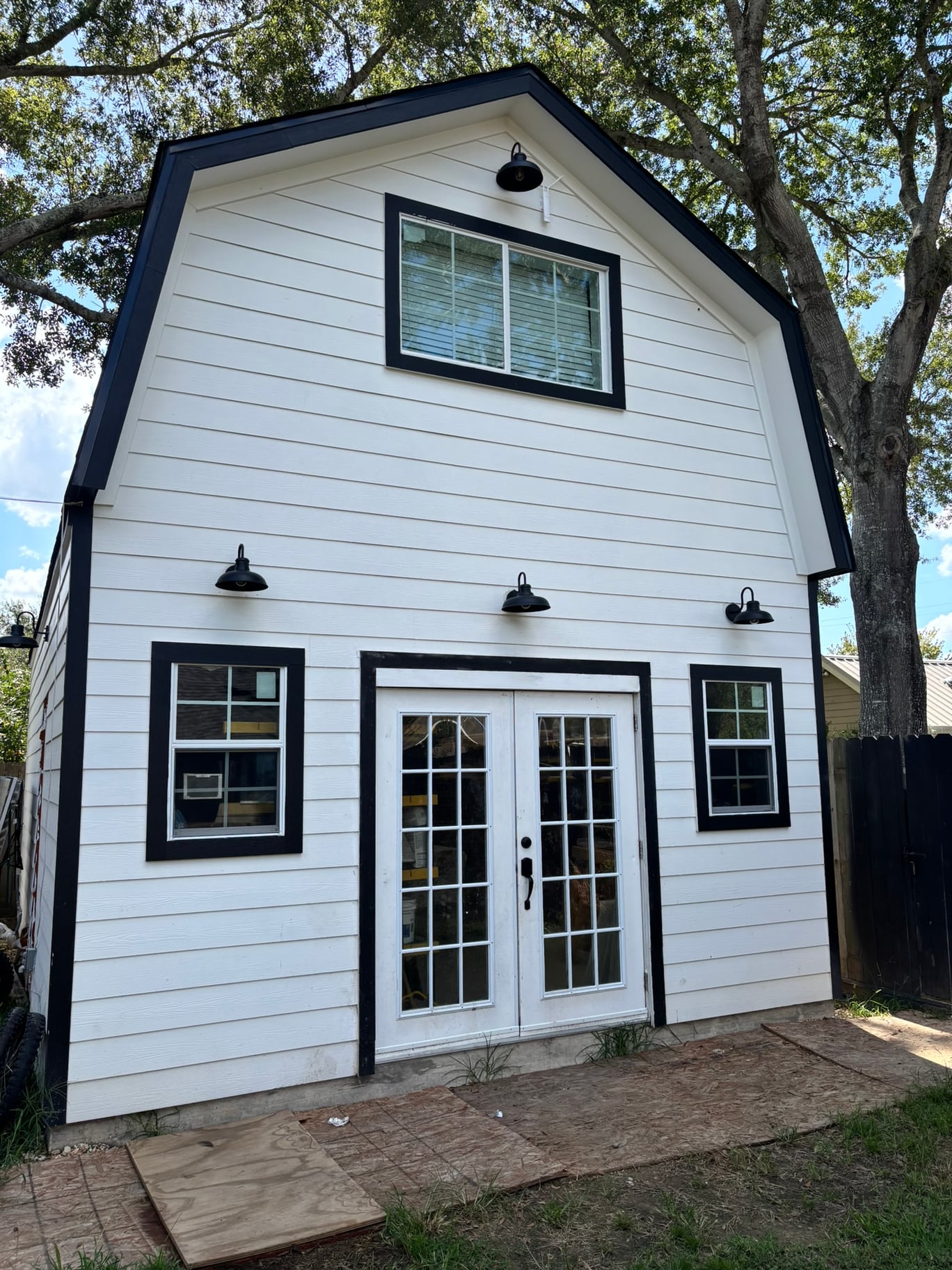 The complete white barn Ben built for his woodworking shop, with black trim and French doors.