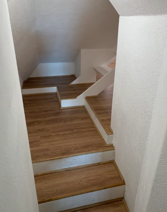 Finished attic entrance with laminate stairs, white walls, and built-in shelving.
