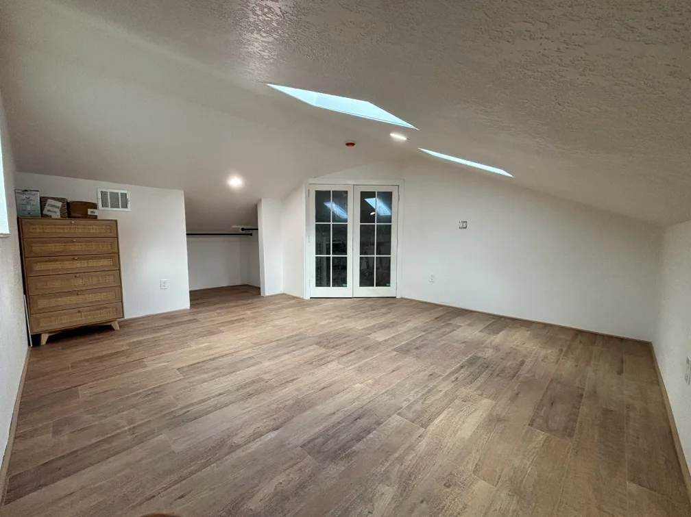 Finished attic room with white walls, skylight, and laminate flooring