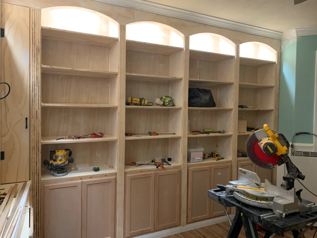 Unfinished built-in library shelves and cabinets surrounding arched windows.