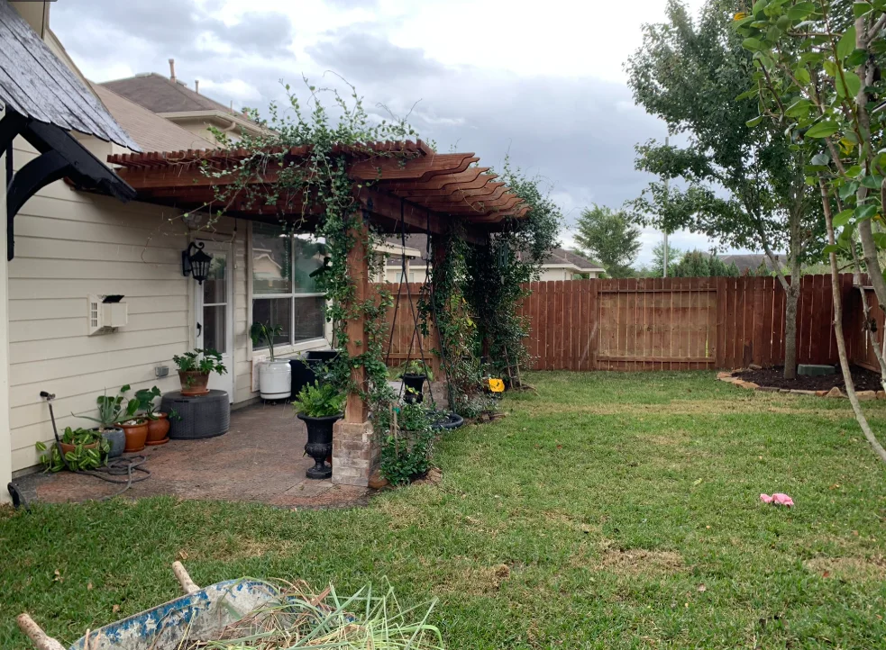 Custom wood pergola anchored along the back of a home over a garden patio.